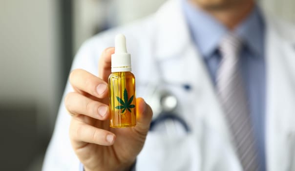 Male doctor hold bottle with marijuana oil medical hospital office closeup. Purpose narcotic drugs concept
