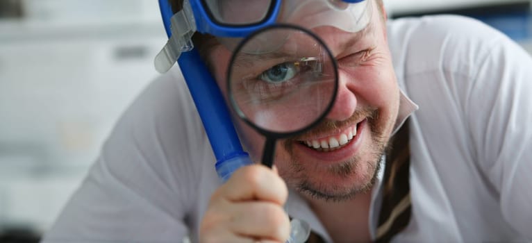 Funny smiling man wearing suit and tie in goggles and snorkel hold in arm magnifier glass at workplace in office portrait closeup. Searching data at online web about tourism 404 page error