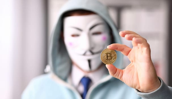 Tbilisi, Georgia, June, 2023: Hacker wear anonymus mask hold bitcoin in hand Illustrative editorial
