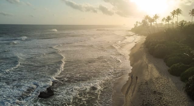 A breathtaking aerial view of a cliff by the ocean at sunset, with the water reflecting the colorful sky and clouds, creating a fluid and natural coastal landscape.