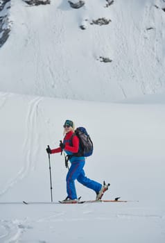 A female skier stands at the snowy summit of a mountain, equipped with professional gear and skis, poised for an exhilarating descent