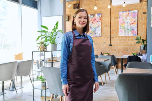 Attractive successful young woman service worker, business owner in apron looking at camera in restaurant cafeteria coffee pastry shop interior. Small business staff occupation entrepreneur work