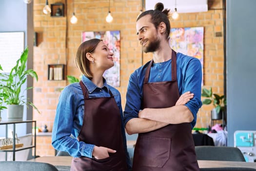 Small business team, successful colleagues partners workers young man and woman in aprons talking at workplace in restaurant coffee shop cafeteria. Cooperation, partnership, teamwork, staff, work