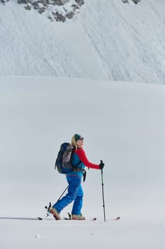 A determined skier scales a snow-capped peak in the Alps, carrying backcountry gear for an epic descent