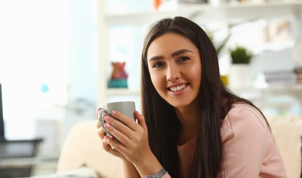 Indian woman holds mug her hand, smiles and lies on the sofa. Work at home education concept.