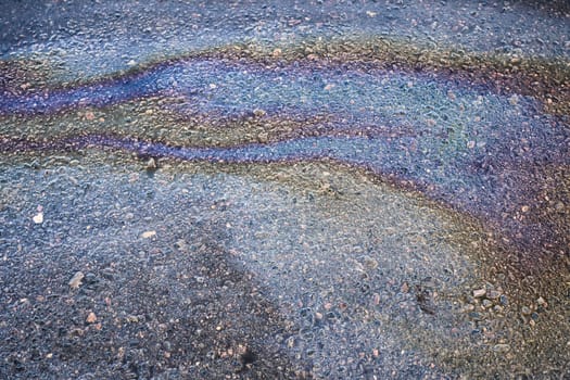 Leakage of oil or gasoline from under the car on the asphalt in the parking lot.