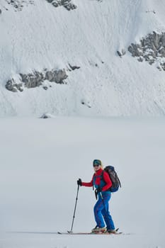 A female skier stands at the snowy summit of a mountain, equipped with professional gear and skis, poised for an exhilarating descent