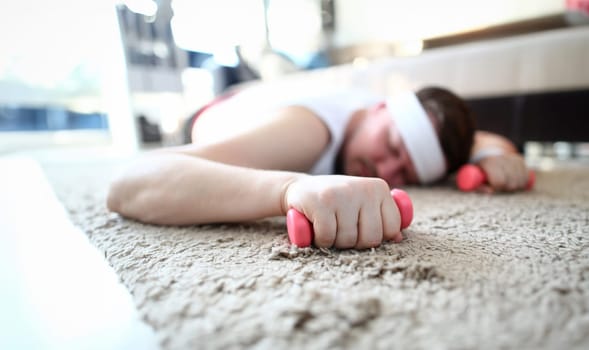 Exhausted Man Sleep and Hold Dumbbells in Hands. Young Male Tired by Fitness Training Lying on Floor in Apartment. Guy with Sports Equipment. Overweight Guy Practice Aerobic for Weight Loss