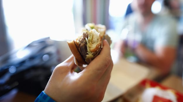 Male hand hold teasty burger in hand aganist cafe background