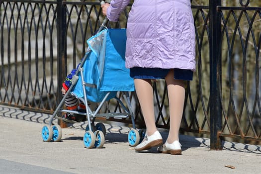 A woman with child in a stroller walks along the fence. Fragment