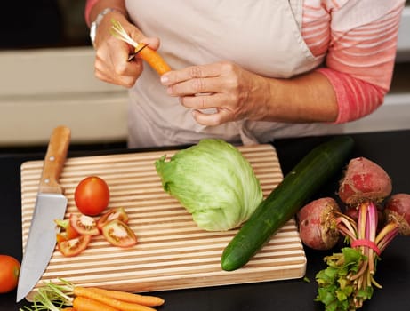 Senior woman or closeup with salad in kitchen and cutting, tomato and carrots for diet. Female chef and zoom with healthy vegetables for nutrition, peeling green lettuce with onion in retirement home.