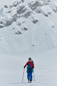 A determined skier scales a snow-capped peak in the Alps, carrying backcountry gear for an epic descent