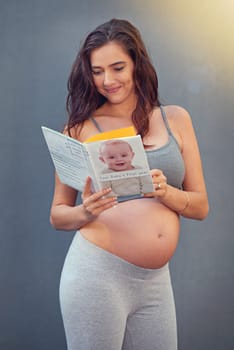 Pregnant woman, baby book and smile in studio for maternity and prenatal wellness for pregnancy and motherhood. Young person, happy and isolated with growing belly and read for childbirth wellbeing.