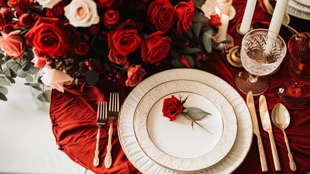 Festive table setting with cutlery, candles and beautiful red flowers in a vase.