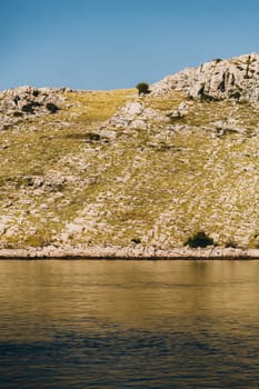 Golden reflection of dry rocky hill on coast of Dugi Otok island in Adriatic Sea, Croatia