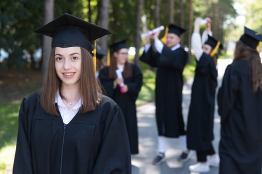 Group of happy students in graduation gowns outdoors. A young girl is happy to receive her diploma