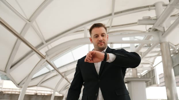 Skilled business man looking watch while walking to train station for going to workplace at bridge. Caucasian manager checking time for important appointment and walk along modern urban city. Urbane.