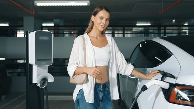Young motion woman travel with EV electric car to shopping center parking lot charging station in downtown city sustainability lifestyle by green clean rechargeable energy of electric vehicle innards