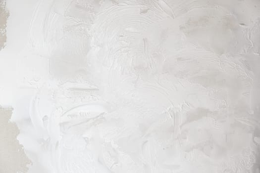 Applying decorative putty. White abstract texture of surface covered with putty. textured background of filler paste applied with putty knife in irregular dashes and strokes. Rough surface plaster