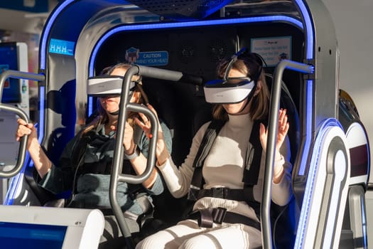 Moscow, Russia, March 14, 2024. Two woman is sitting in an electric blue virtual reality chair, wearing a headset. The machine combines engineering and fun in a display device