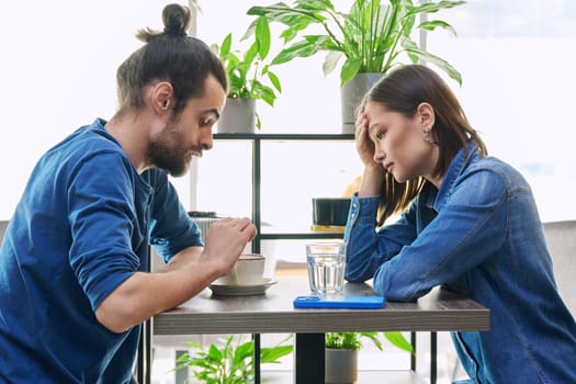 Serious aggressive young couple quarreling, angry, arguing, talking, nervous, sitting together at table in cafeteria. Relationships difficulties problems negative emotions lifestyle people concept