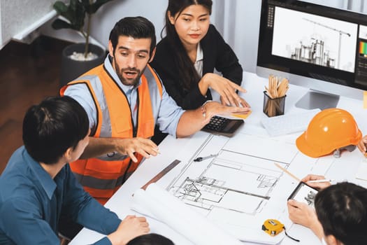 Diverse group of civil engineer and client working together on architectural project, reviewing construction plan and building blueprint at meeting table. Prudent