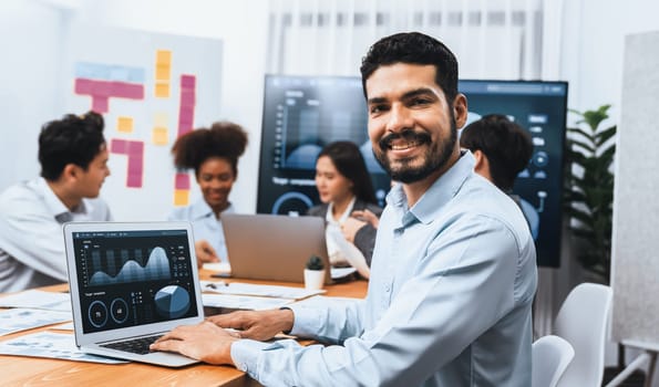 Portrait of happy and smiling businessman with group of coworkers on meeting with screen display business dashboard in background. Confident office worker at team meeting. Concord