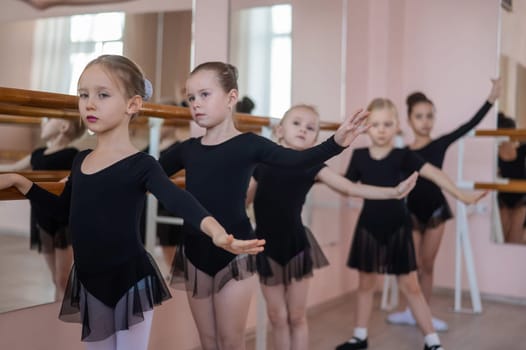 Cute little girls in black swimsuits and tutu do ballet at the barre