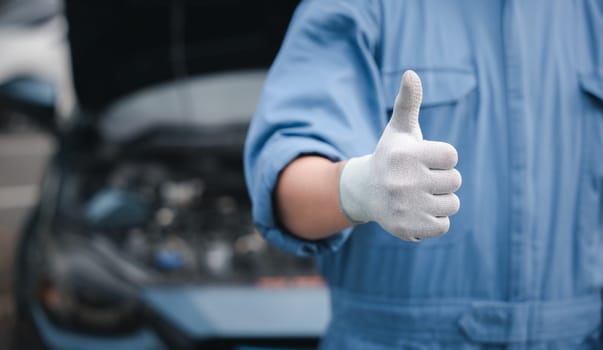 Mechanic in jumpsuit checks car gives thumbs up. Expertise in repair and service ensuring safety and quality. Skilled technician working in automotive industry smiling.