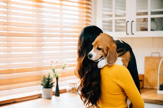 A woman, her Beagle dog on her shoulder, stands in the kitchen interior, emotionally embracing her furry friend. Their close bond, trust, and consoling radiate happiness and joy.