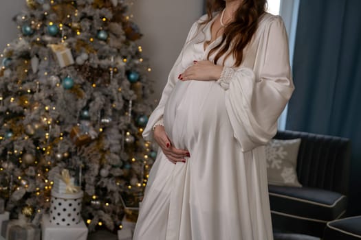 Pregnant woman holding a belly against Christmas tree with lights. family holiday concept