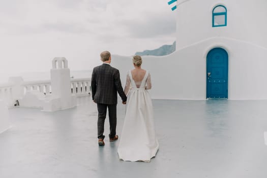 A bride and groom are walking down a path in front of a blue door. The bride is wearing a white dress and the groom is wearing a suit. Scene is romantic and happy