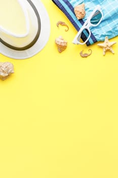 Beach hat with shorts and sunglasses on yellow isolated background. Flat lay. Summer vacation concept. Top view. Starfish and seashells. Vertical photo.