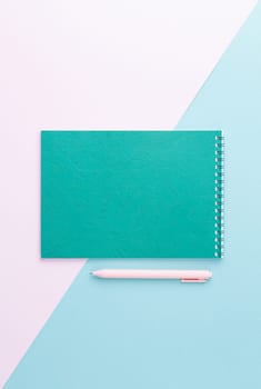 Green spiral notebook with pink pen on two color isolated background. Top view. Office concept.