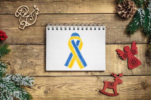 ukrainian yellow and blue ribbon in the middle of a notebook on a wooden christmas background. concept needs help and support, truth will win