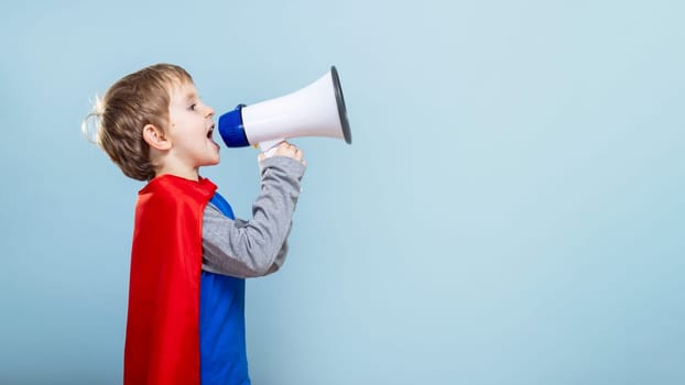 Young boy in superhero costume shouting into megaphone. Studio portrait with solid blue background. Empowerment and imagination concept. Design for banner, poster, invitation.