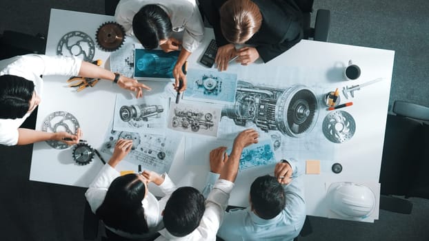 Top down aerial view of smart engineer team working together to design turbine engine. Professional technician discussing about jet engine construction while pointing at part of engine. Alimentation.