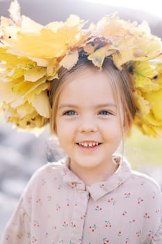 Little smiling girl wearing a crown of yellow leaves. Portrait. High quality photo