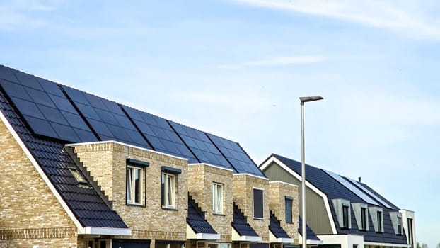 Dutch Suburban area with modern family houses with black solar panels on the roof against a sunny sk,. Zonnepanelen, Zonne energie, Translation: Solar panel, Sun Energy