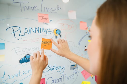 Closeup of professional businesswoman hand put and stick the colorful sticky notes on whiteboard while presenting business plan. Creative business meeting and brainstorming concept. Immaculate.