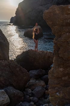 Woman tourist enjoying the sunset over the sea mountain landscape. Sits outdoors on a rock above the sea. She is wearing jeans and a blue hoodie. Healthy lifestyle, harmony and meditation.