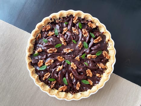 Homemade tart with pear and dark chocolate in a white baking dish, natural light.