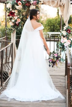 Bride, back and summer wedding with flowers, romance and celebration for social event. Woman, bouquet and promise for communion, commitment and bridal ceremony for elegant milestone with beauty.
