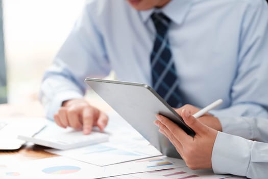 Close-up of a businessman's hands using a stylus on a tablet over financial charts for business analysis.