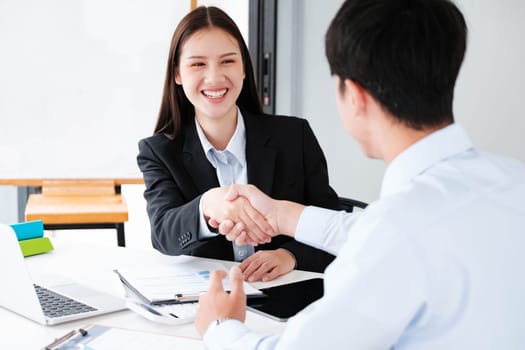 A young businesswoman smiles while shaking hands, making a positive impression during a professional meeting.