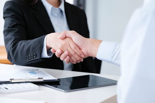 Close-up of a professional handshake between colleagues sealing a business deal, with work documents and tablet in background.
