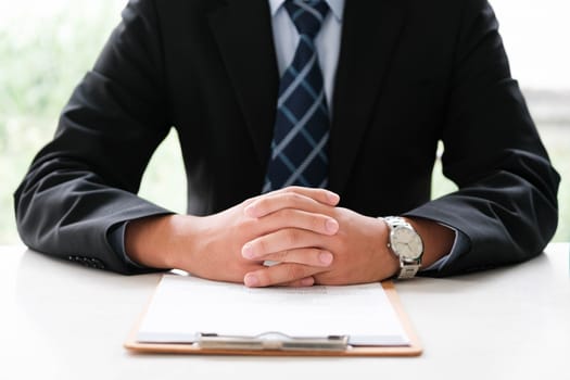 Professional Executive in Business Attire with Hands Clasped over Document, Signifying Preparedness and Confidence in a Corporate Setting