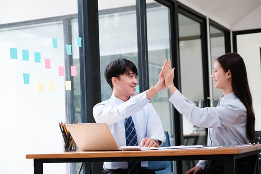 Two elated business colleagues giving a high-five over a successful project at their office workspace.