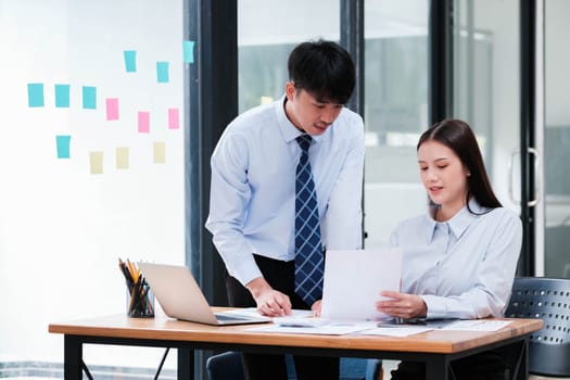 Asian business colleagues in discussion over digital and paper data analysis for company growth strategy at an office desk.