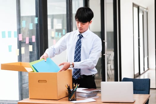 A man in a suit is opening a cardboard box on a desk. The box contains papers and a laptop